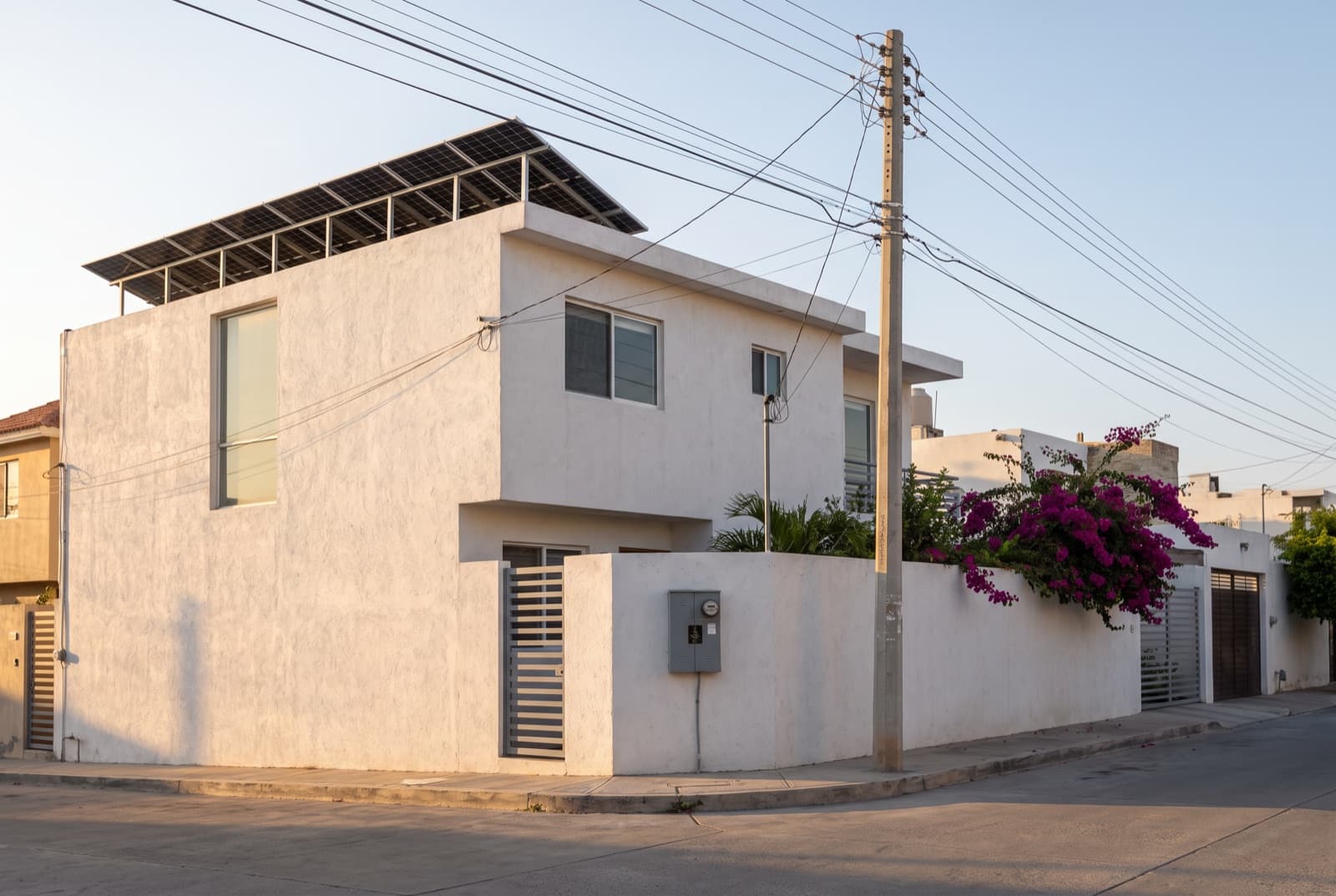 Casa con paneles solares en la azotea, con su medidor y la acometida de la red eléctrica